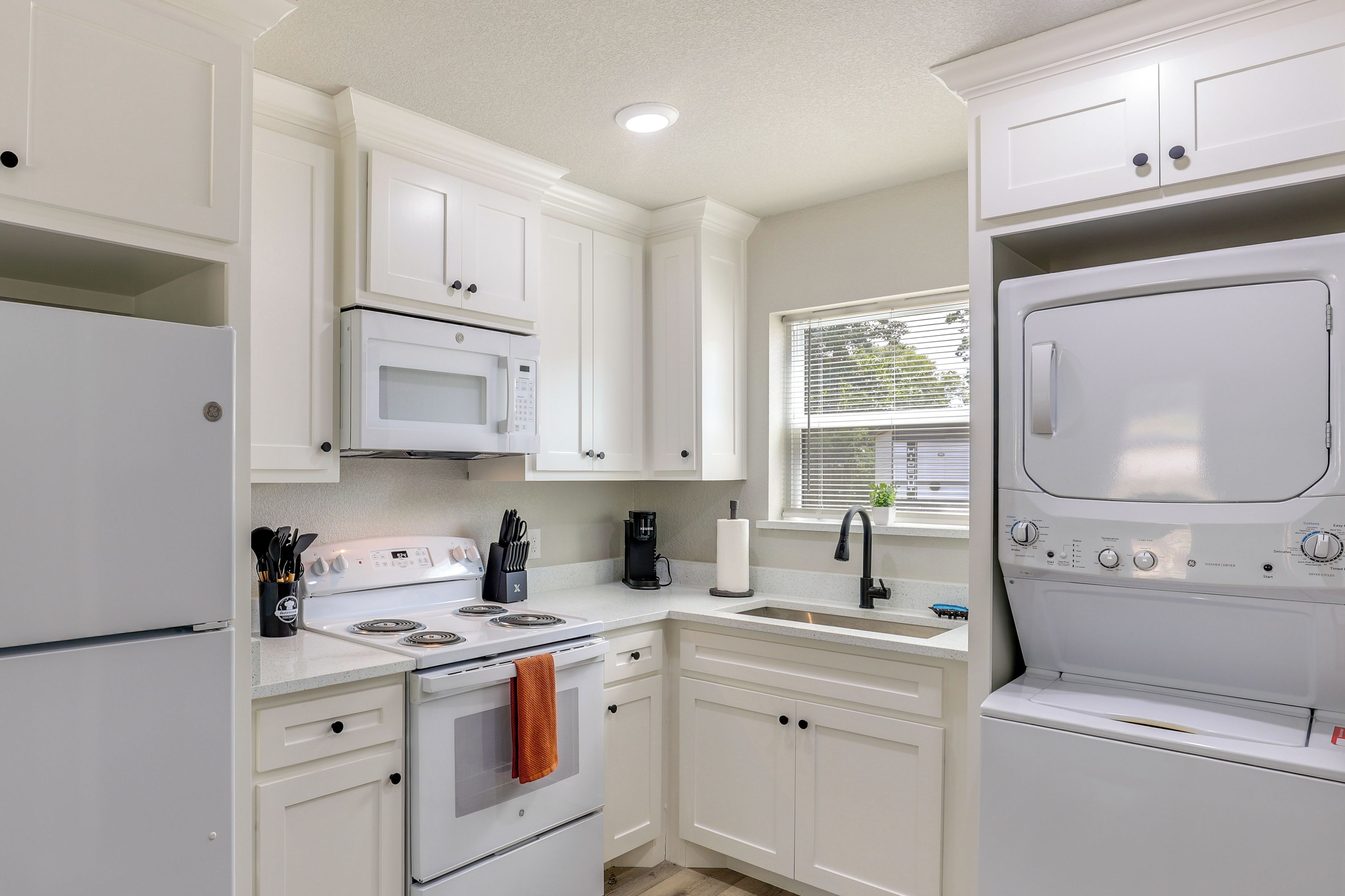 A modern kitchen with white cabinetry, a built-in microwave, a stove, and a washer-dryer unit.