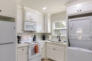 Una cocina moderna con muebles blancos, un microondas integrado, una estufa y una lavadora-secadora.