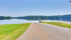 A paved pathway leading to a calm lake with a grassy area on one side and a forested hill on the other. - Orchard, Pond On-site! Farm Stay Near Point A Lake (Red Level)