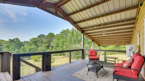 A covered outdoor deck with a view of a wooded area, furnished with two red chairs and a table. - Orchard, Pond On-site! Farm Stay Near Point A Lake (Red Level)