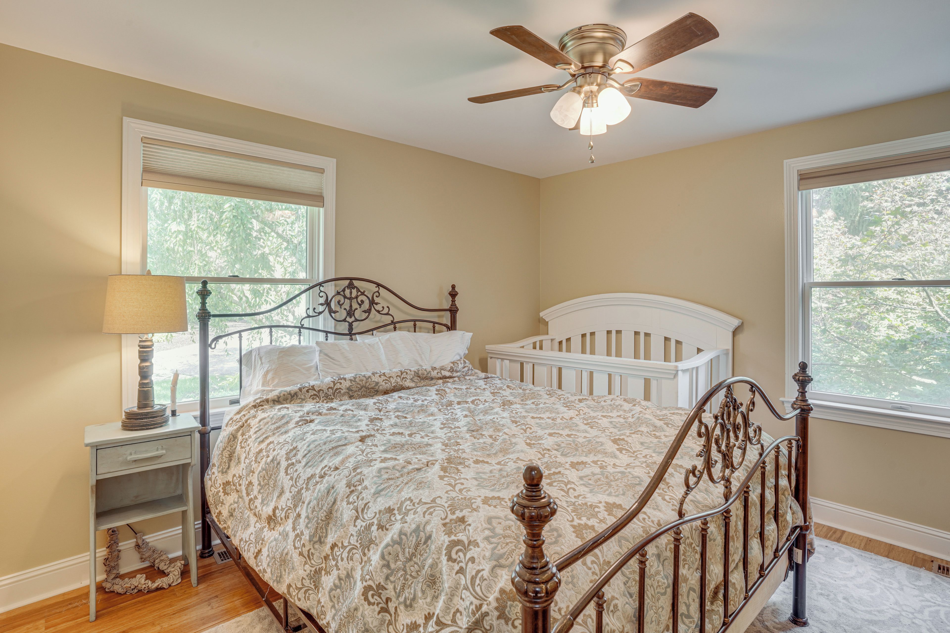 A bedroom with a bed, a nightstand, a lamp, a ceiling fan, and two windows.