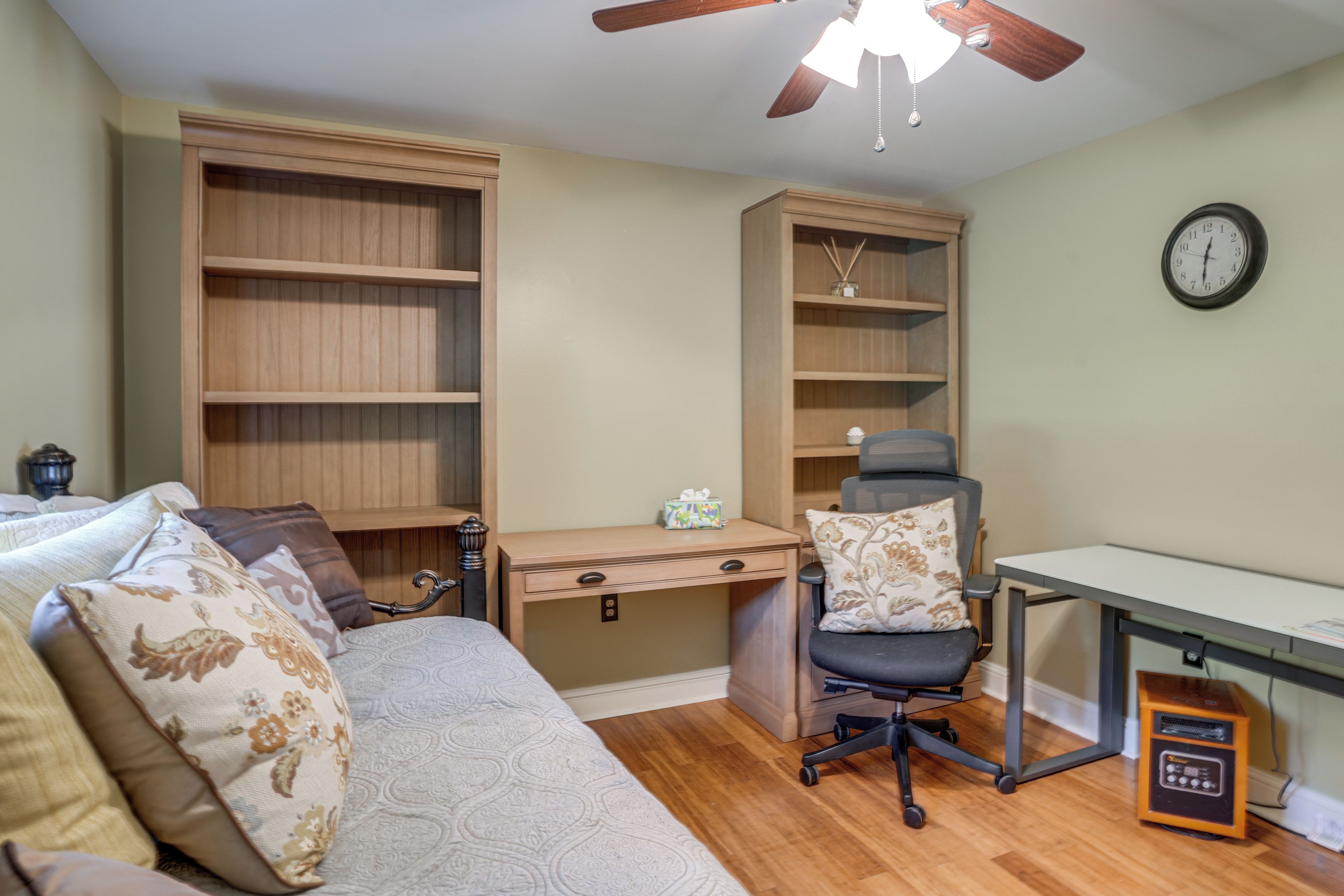 Een slaapkamer met een bed, een bureau, een stoel en een boekenplank.