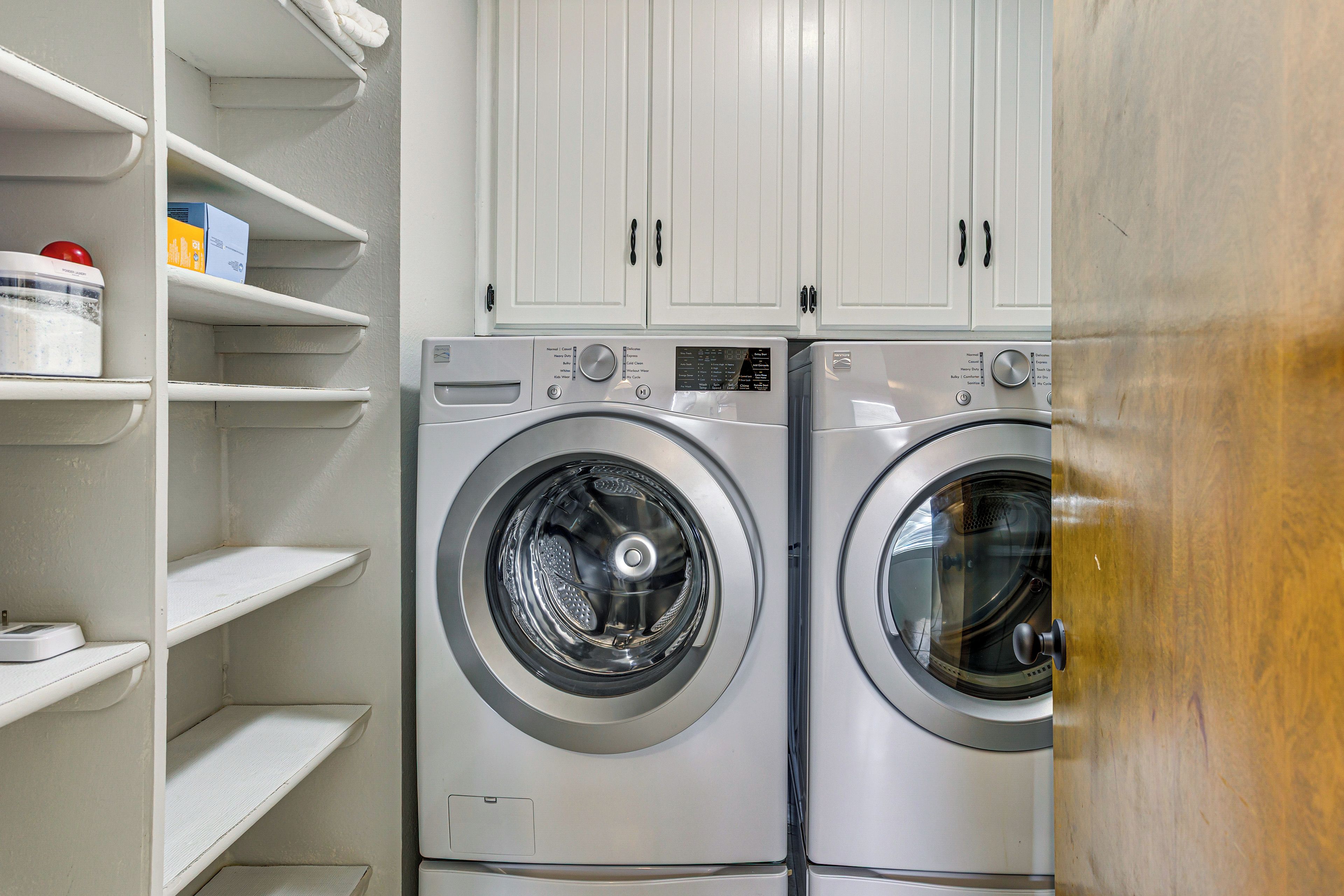 A laundry room with two front-loading washing machines and white cabinets above.