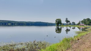 A calm lake with a clear sky, surrounded by trees and a small building with a red roof. - Boating & Fishing Base! Studio Near Point A Lake (Red Level)