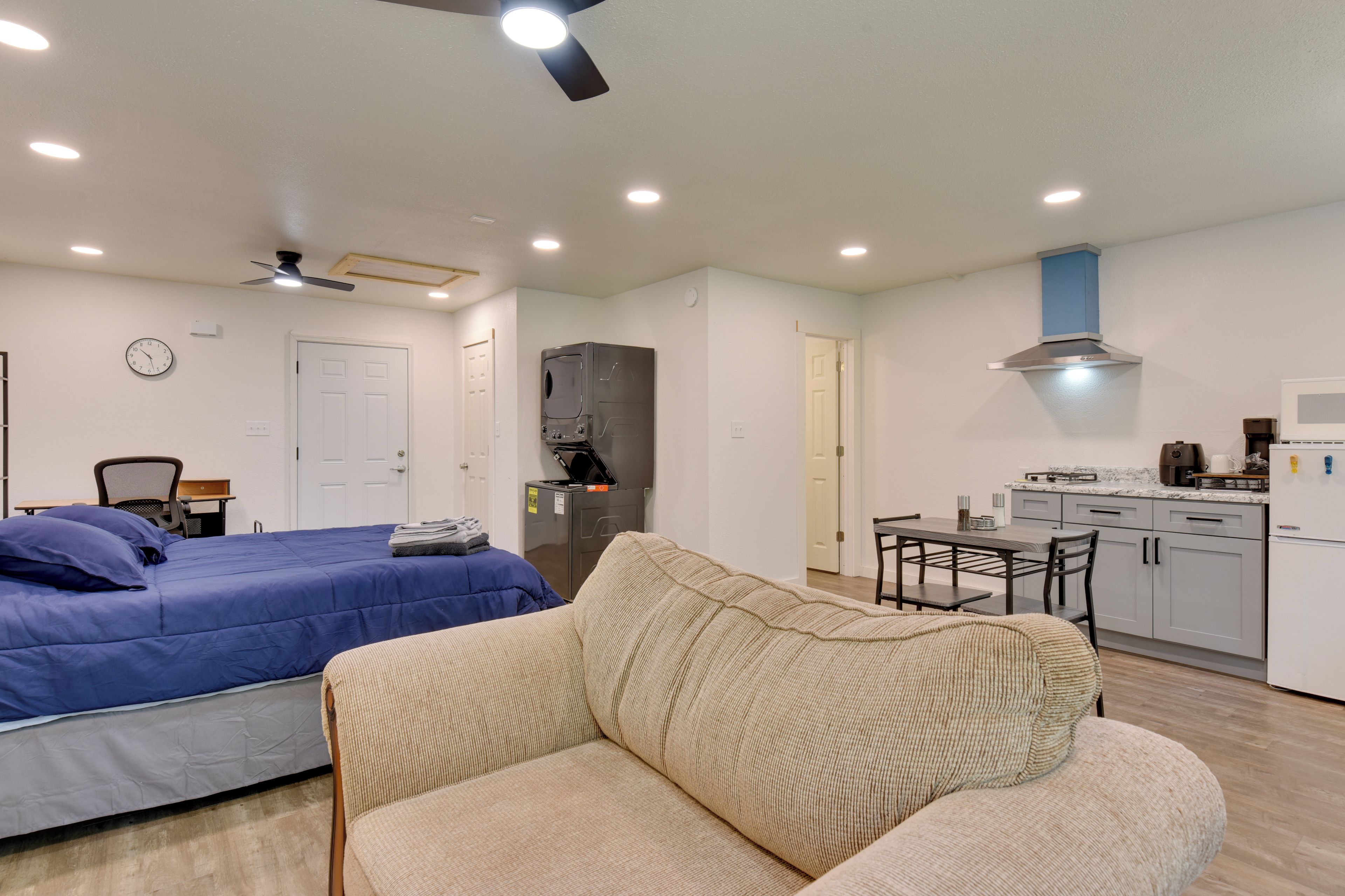 A compact living space with a bed, a sofa, a kitchenette, and a ceiling fan.