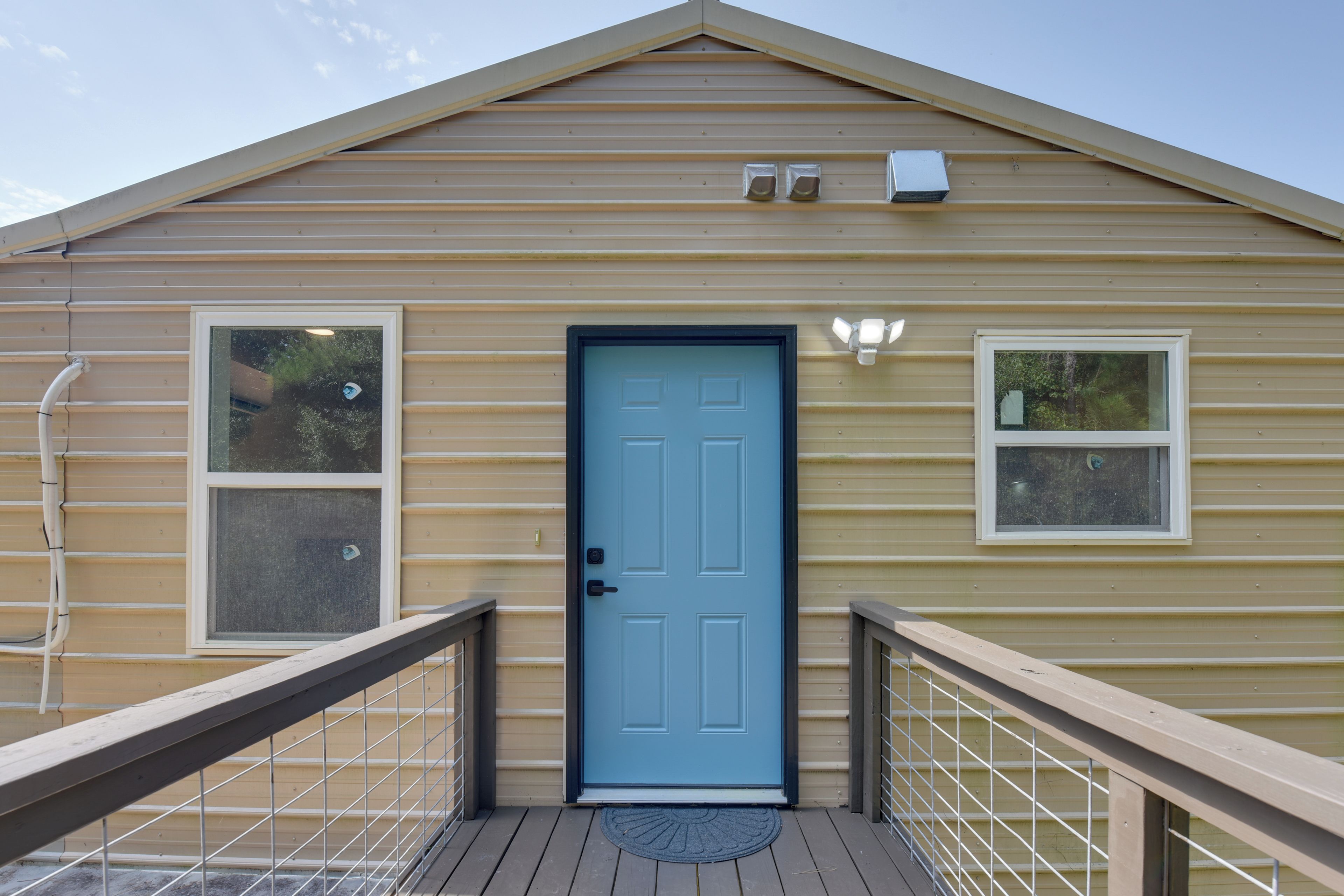 A single-story building with a blue door, two windows, and a small porch with a railing.