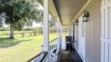 A covered porch with a view of a grassy landscape and trees.