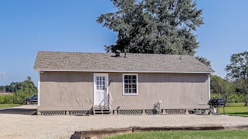 A small wooden building with a door and windows, a chimney, and a gravel driveway.