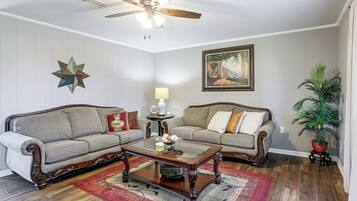 A living room with two sofas, a coffee table, a ceiling fan, a star decoration, a painting, a lamp, and a potted plant.