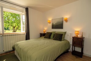 Una camera da letto con un letto, due comodini, una finestra con tende, un termosifone e un quadro appeso al muro.