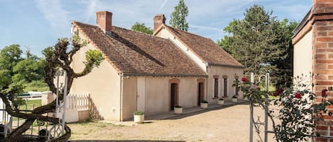 A traditional building with a tiled roof, a gravel courtyard, and a white fence.
