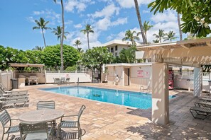 A swimming pool with lounge chairs and a table, surrounded by palm trees and a building. - Newly Renovated | Ground-Floor 1BR Kihei Condo (Kihei)