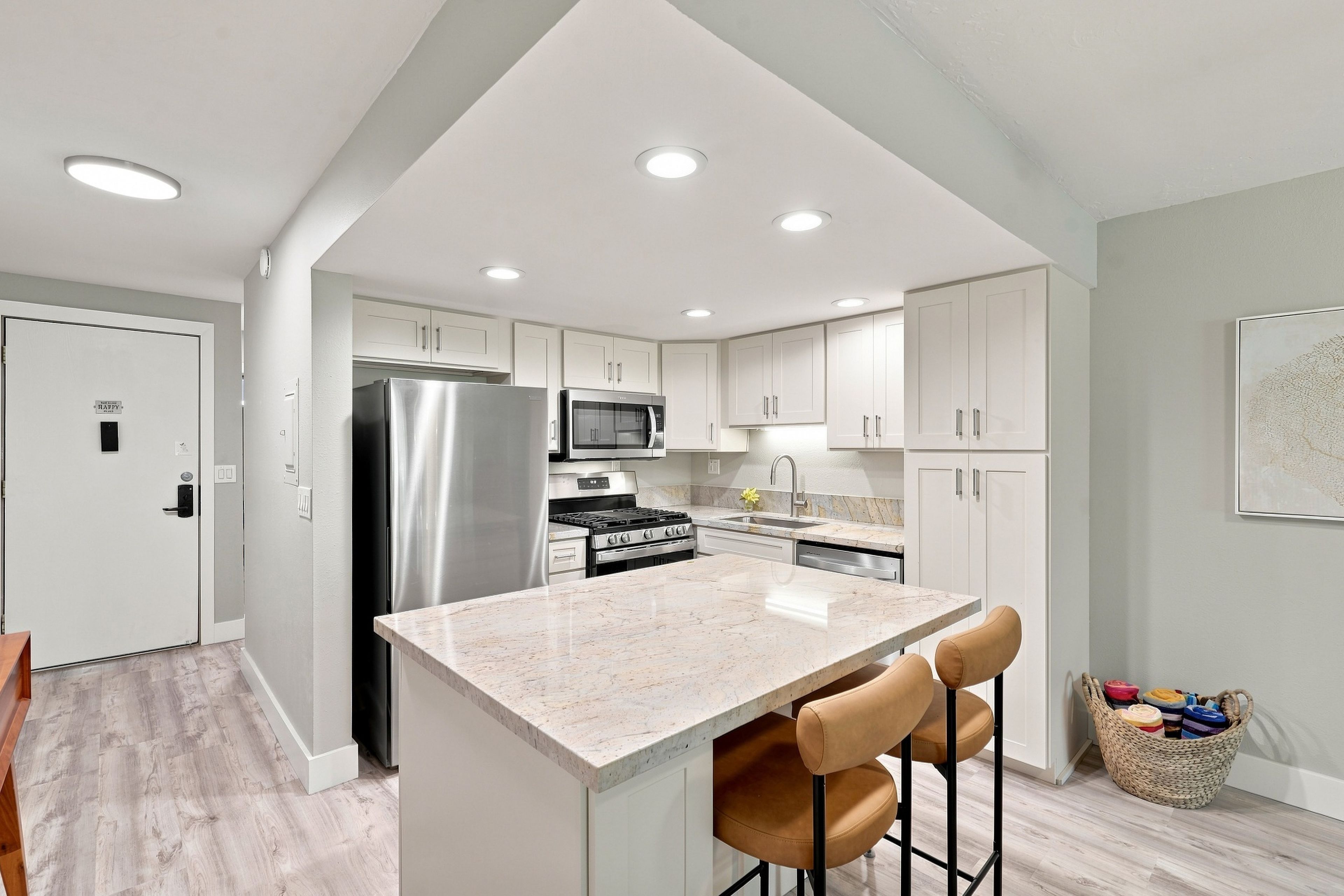 A modern kitchen with a central island, stainless steel appliances, and a light-colored marble countertop.