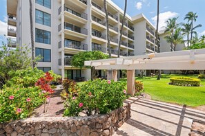Ein mehrstöckiges Hotel mit Balkonen, einem Gartenbereich mit verschiedenen Pflanzen und einem gepflasterten Weg.