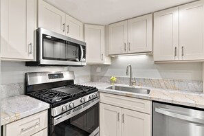 A modern kitchen with stainless steel appliances, white cabinetry, and a granite countertop. - Newly Renovated | Ground-Floor 1BR Kihei Condo (Kihei)