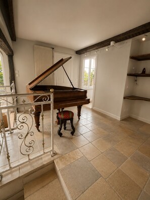 A grand piano in a spacious room with tiled flooring and a staircase leading to an upper level. - The Country House (Bresles)