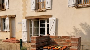 Ein Grill aus Ziegelsteinen im Freien mit verschiedenen Fleisch- und Gemüsesorten, ein Schneidebrett mit Gemüse und ein Blumentopf.