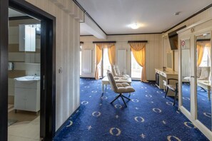 Habitación de hotel con un espejo grande, un escritorio, una silla y una alfombra azul con diseño circular.
