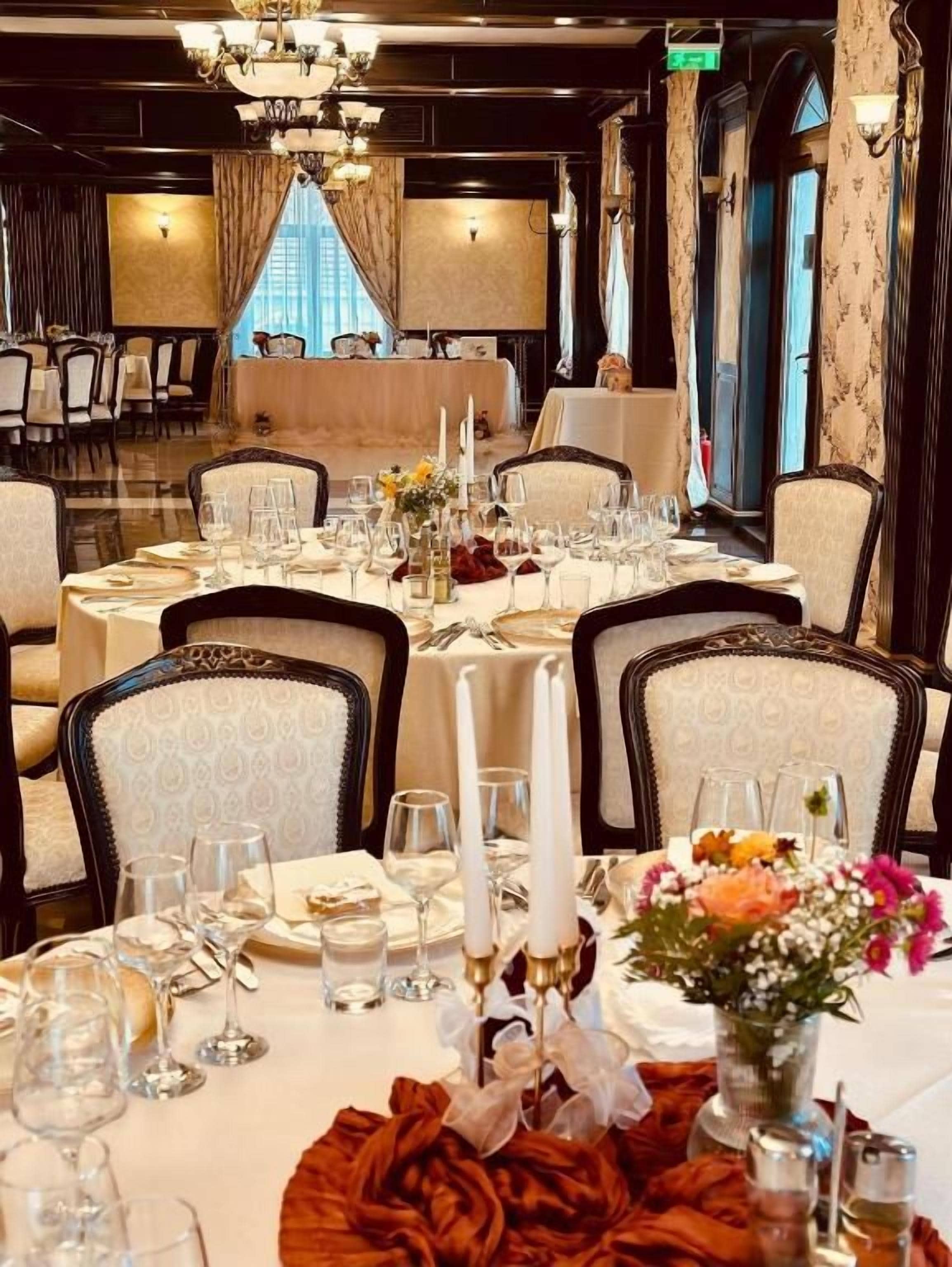 A formal dining room with tables set for a meal, chairs, and a chandelier.