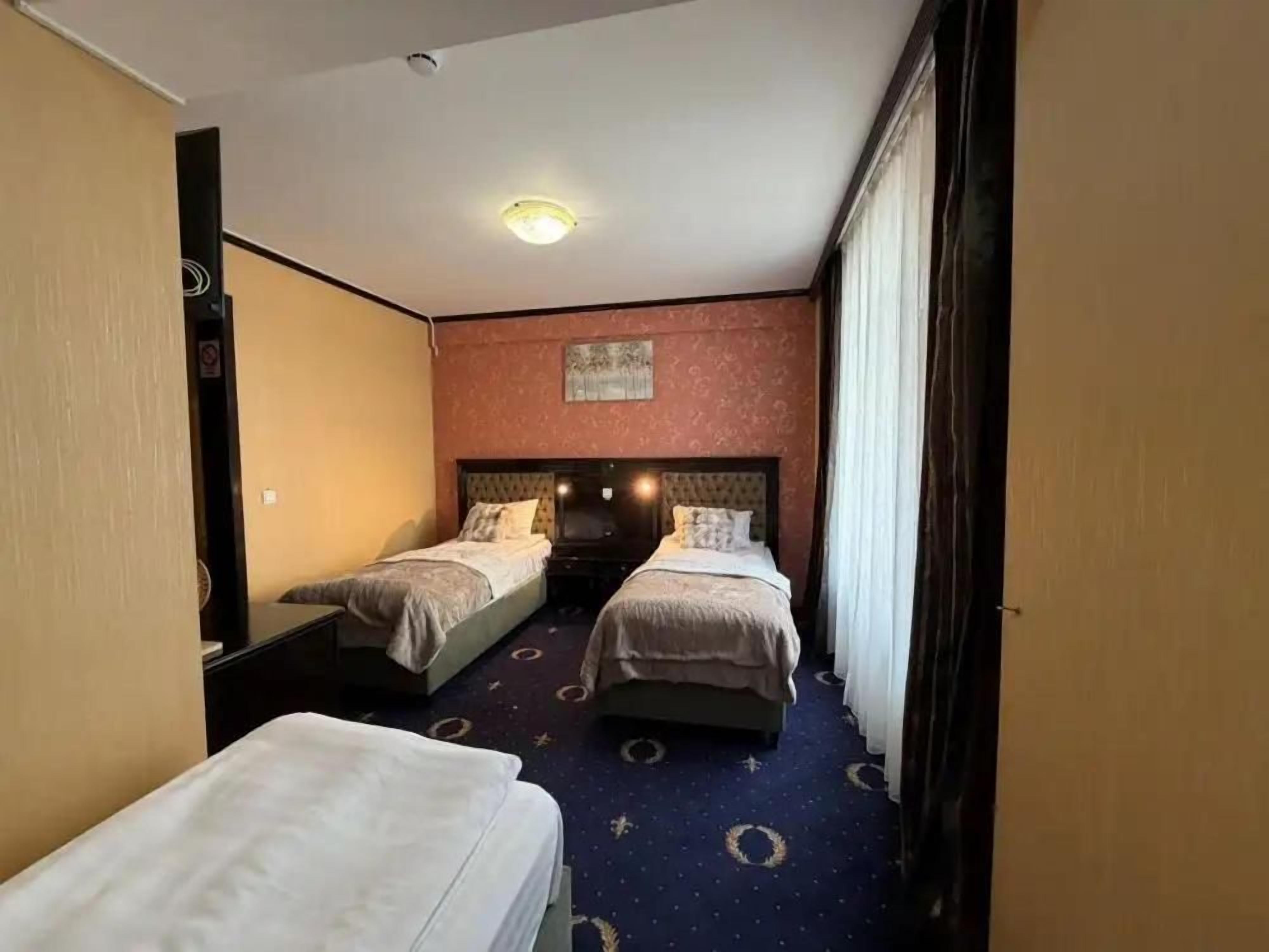 Una habitación de hotel con dos camas individuales, una mesita pequeña, una mesita de noche y una lámpara en el techo.