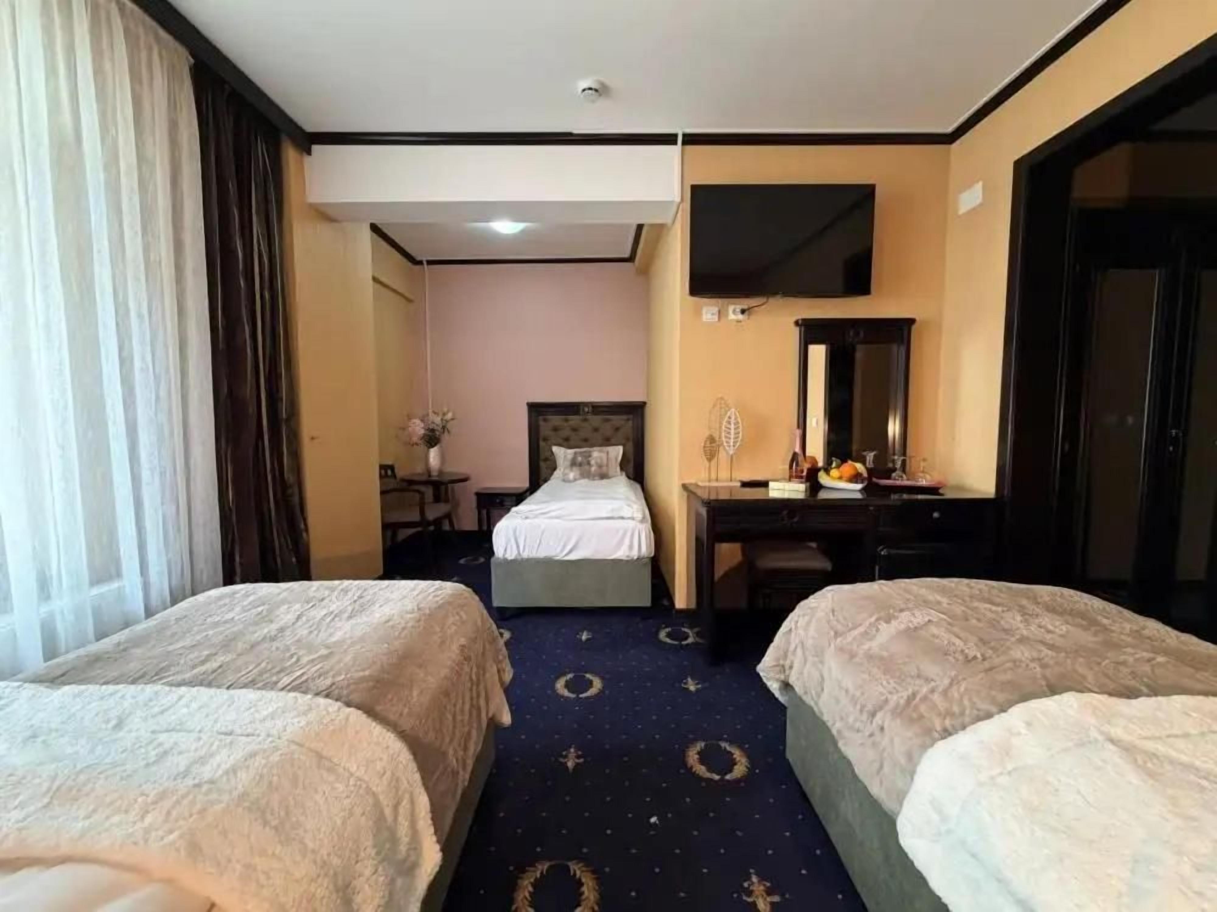 Habitación de hotel con dos camas, un escritorio, televisión y un baño visible a través de una puerta abierta.