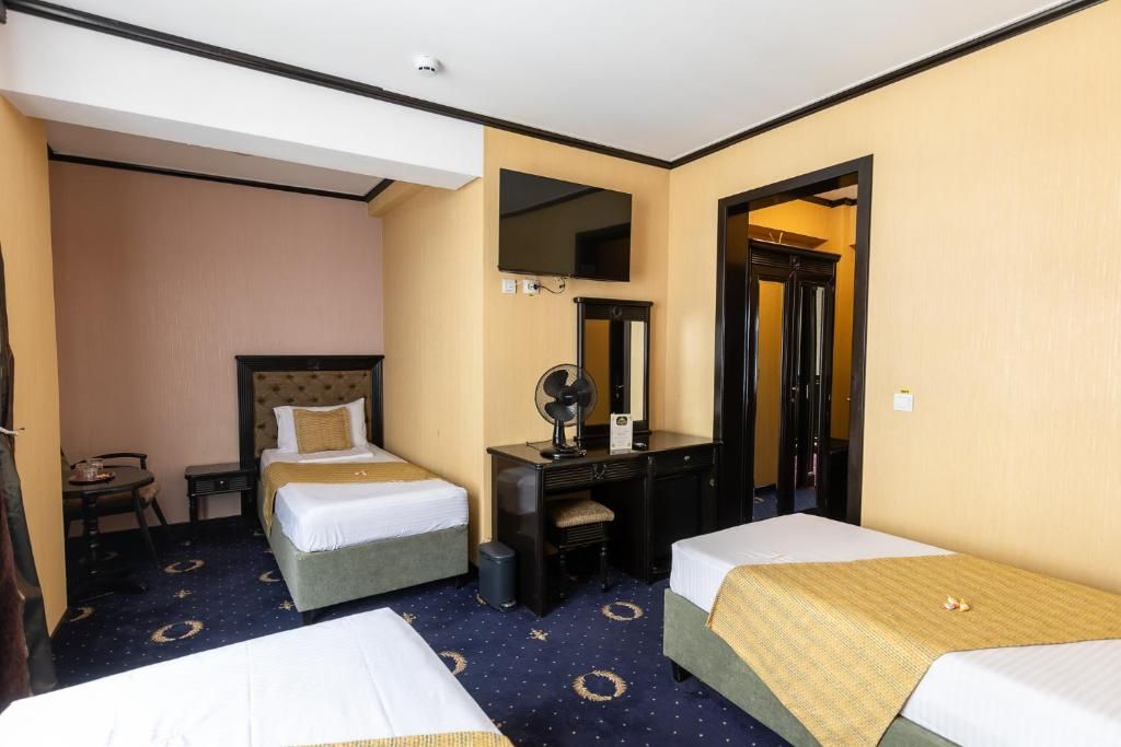 A hotel room with two beds, a desk with a chair, a mirror, and a television.