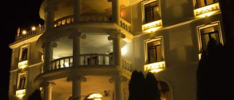 Um edifício com vários andares, varandas, colunas e janelas iluminadas à noite.
