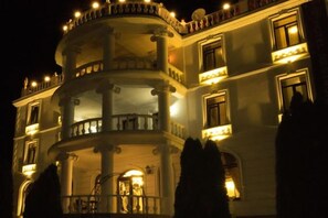 Un edificio de varios pisos con balcones, columnas y ventanas iluminadas durante la noche.