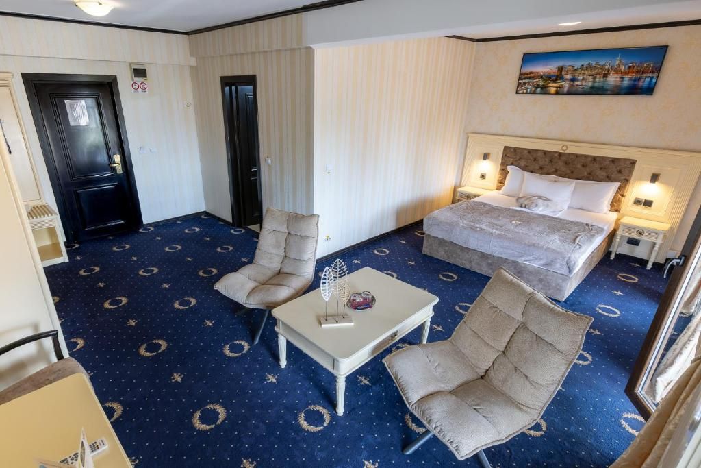 A hotel room with a bed, two armchairs, a small table, and a painting on the wall.