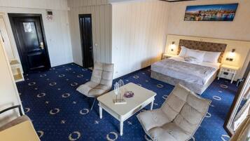 A hotel room with a bed, two armchairs, a small table, and a painting on the wall.