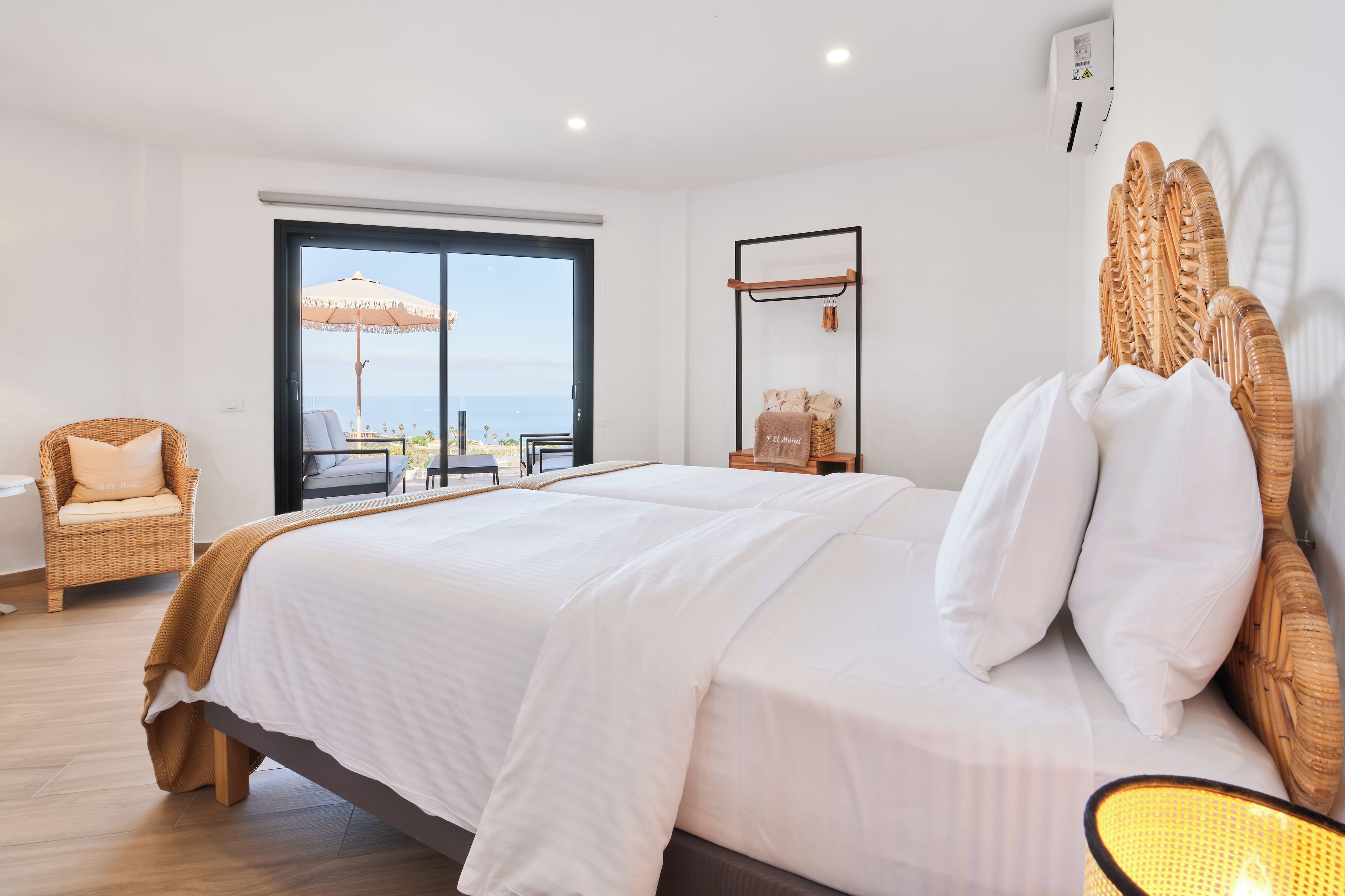 Una habitació amb un llit gran, una cadira de vimet, una taula petita i vista al mar a través d'una porta corredissa.