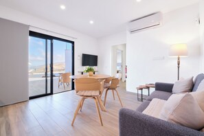 A modern living room with a sofa, a dining table, and chairs. There is a TV mounted on the wall and a lamp on a side table. - Finca el Moral  (Los Llanos)