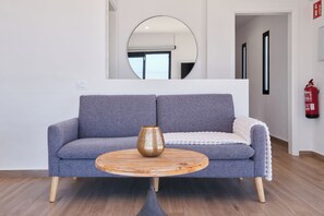 Ett modernt vardagsrum med en grå soffa, ett soffbord i trä och en stor spegel på väggen.