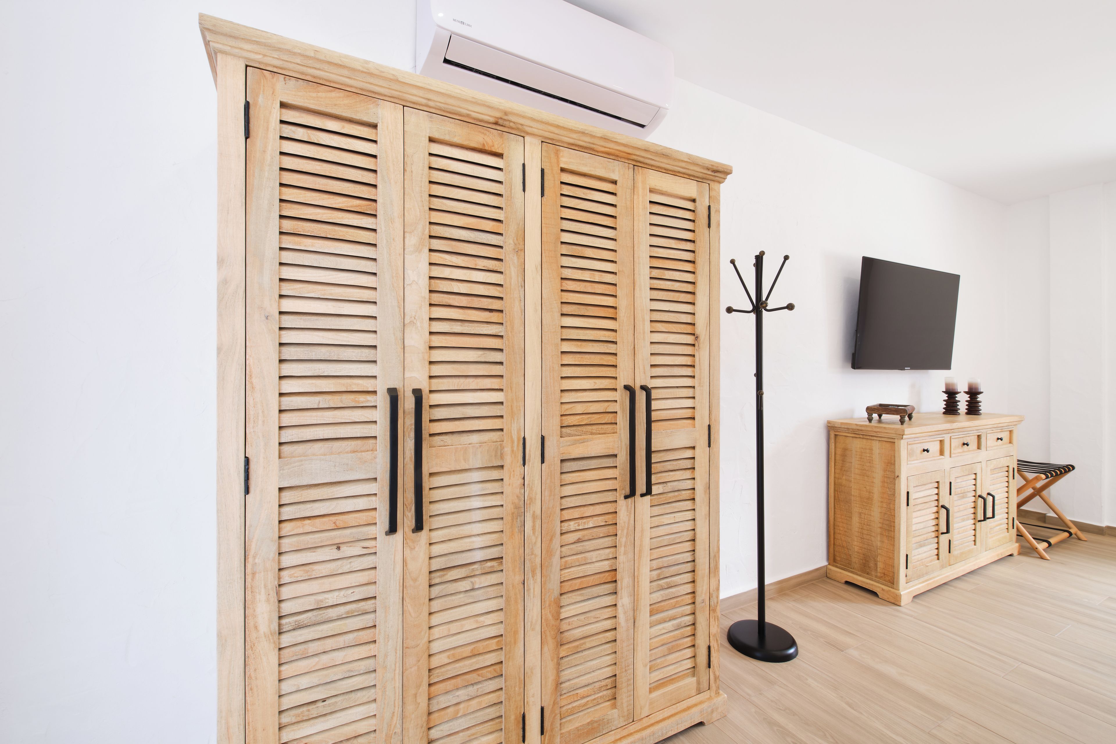 A room with a wooden wardrobe, a flat-screen TV, and a coat rack.