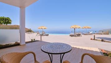 An outdoor seating area with a view of the ocean, featuring wicker chairs, a round table, and thatched umbrellas.