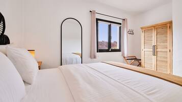 A bedroom with a bed, a mirror, a window with a view, a wooden wardrobe, and a chair.