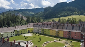A courtyard with a circular lawn, a small garden area, and a row of multi-story buildings with a consistent architectural style. - Apartment in Eisenerz With Sauna and Balcony (Eisenerz)