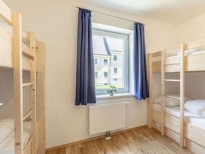 Une chambre avec des lits superposés, une fenêtre avec des rideaux, un radiateur et une vue sur les bâtiments à l’extérieur.