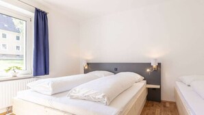 A bedroom with a bed, a nightstand, a window with curtains, and a view of buildings outside. - Apartment in Eisenerz With Sauna and Balcony (Eisenerz)
