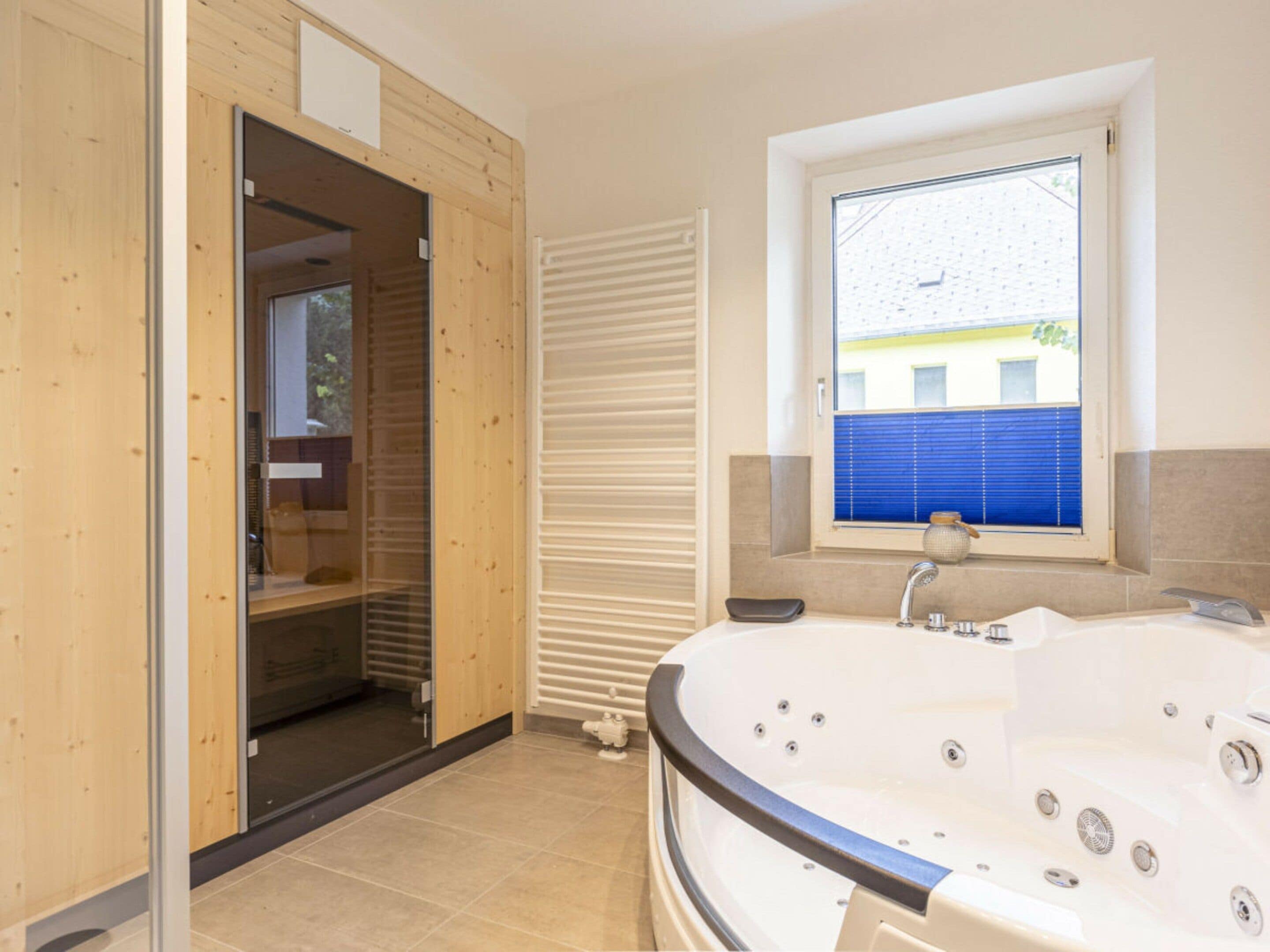 Une salle de bain avec une grande baignoire, une fenêtre avec des stores et une porte en bois donnant sur une autre pièce.