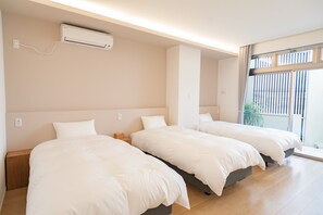A hotel room with three single beds, a ceiling air conditioner, and a large window with blinds. - 30-second walk to the beach. Stay like you're living here. Stunning sunset and ocean views. Beachside Island Home, Steps from the Sea (Miyakojima)