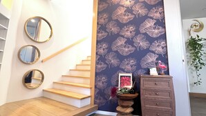 Una escalera con escalones de madera y una pared con estampado floral. Hay tres espejos redondos en la pared, un pequeño aparador de madera y un cuadro enmarcado con flores.