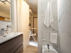 Une salle de bain moderne avec un mur en marbre, un lavabo blanc, un miroir et un porte-serviettes.