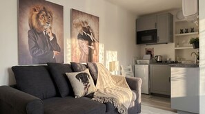 Un salon moderne avec un canapé gris, deux coussins décoratifs et une cuisine en arrière-plan.