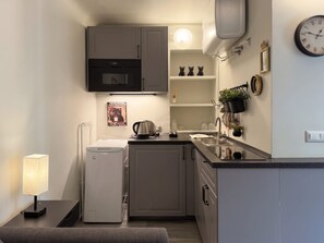A compact kitchen with a microwave, kettle, and sink. There is a clock on the wall and a small shelf with decorative items. - The 6th - Studio Apartment Porta Venezia (Milano)