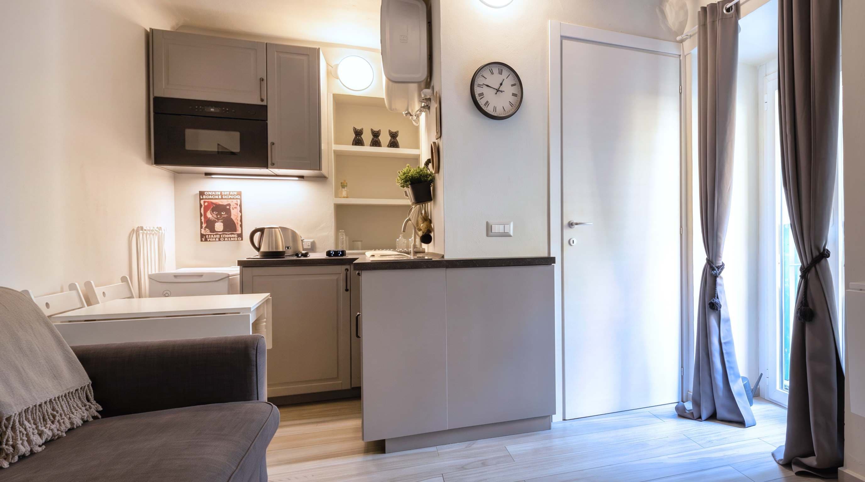 A compact kitchen with a clock, a dining area with a table and chairs, and a living space with a sofa.
