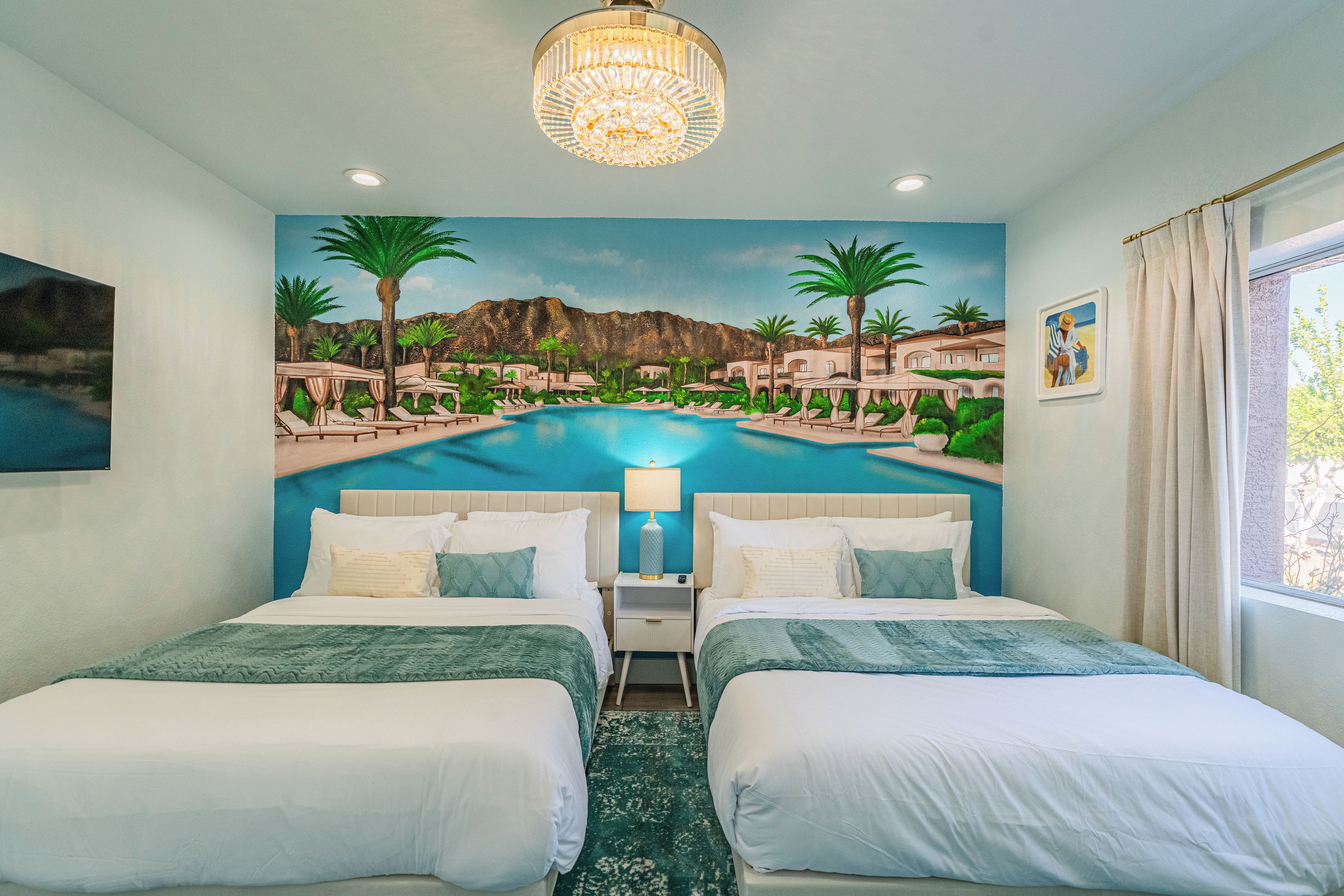 A hotel room with two beds, a mural of a pool and palm trees, a chandelier, and a window with curtains.