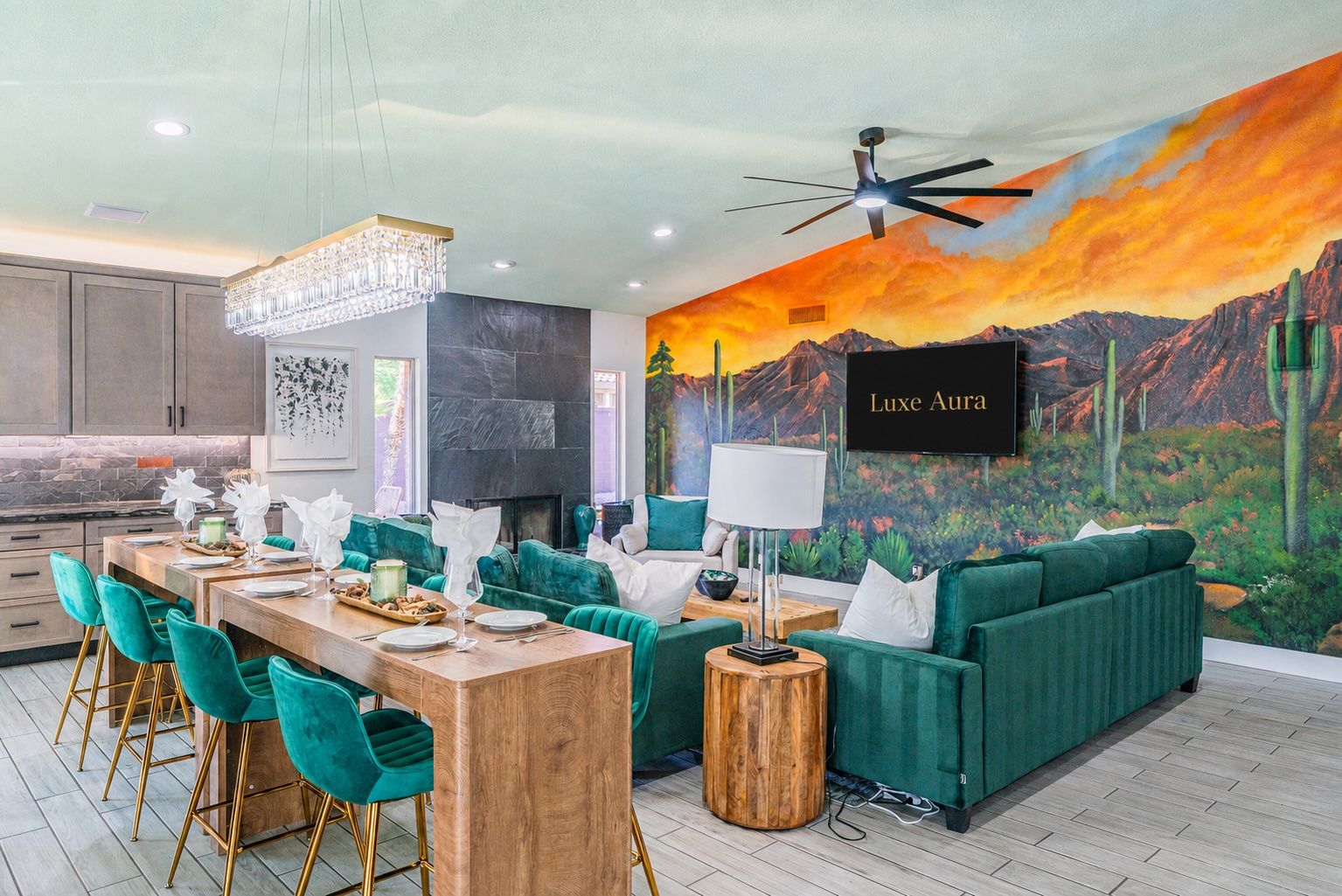 A modern interior with a dining area, green sofas, a chandelier, and a mural of a desert landscape.