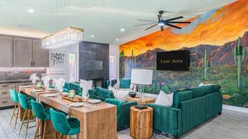 A modern interior with a dining area, green sofas, a chandelier, and a mural of a desert landscape.