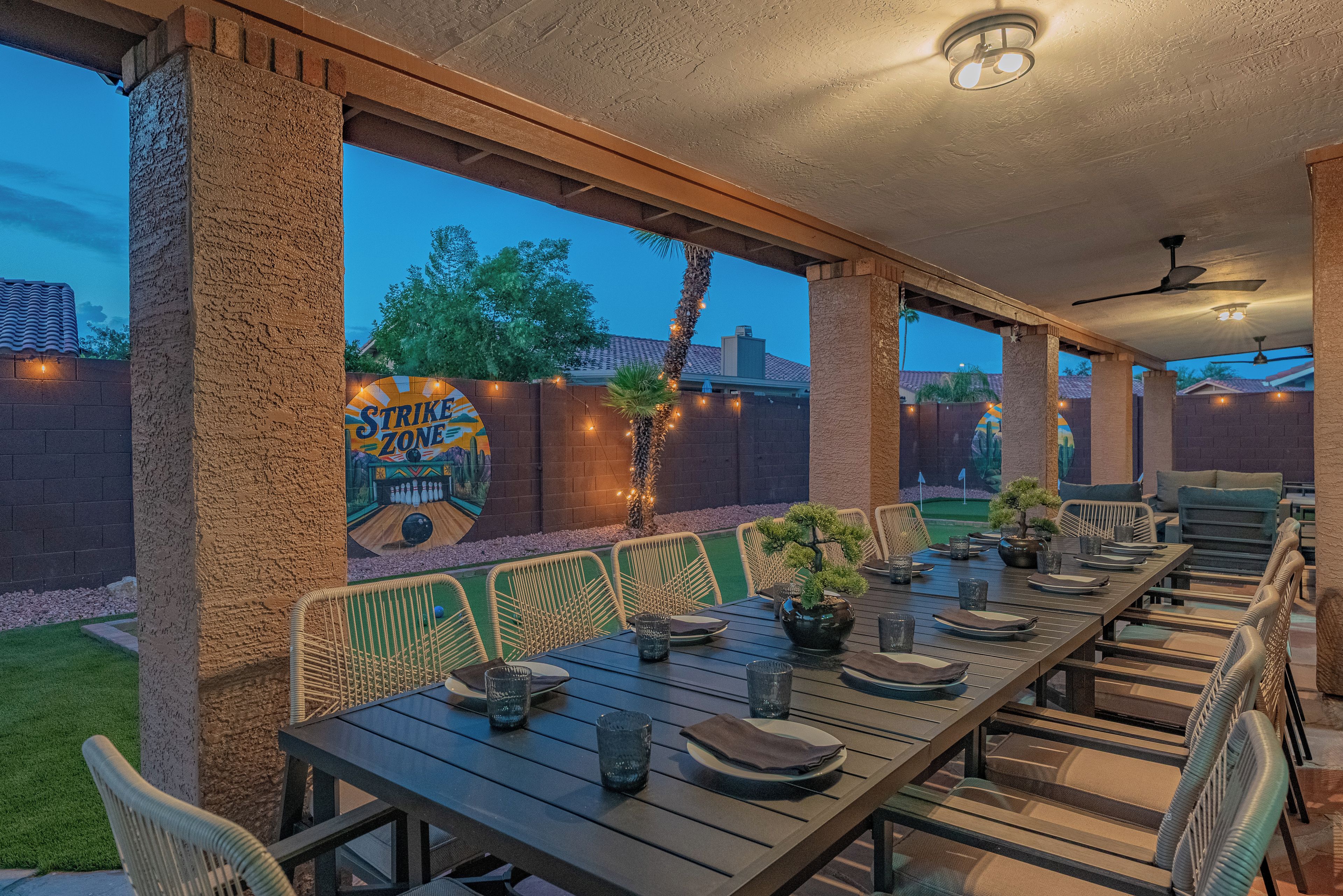 An outdoor patio with a bowling alley mural, dining tables, chairs, and string lights.